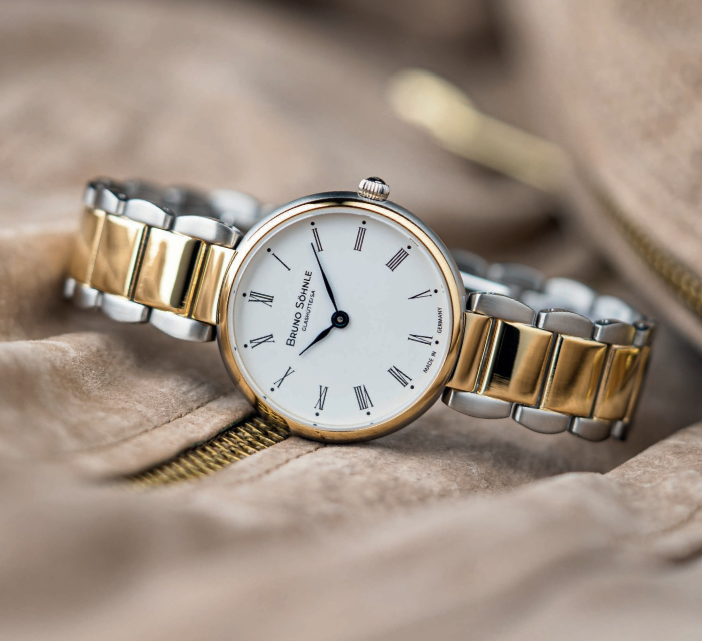 Eine silberne und goldene Uhr liegt auf einem braunen Tuch.