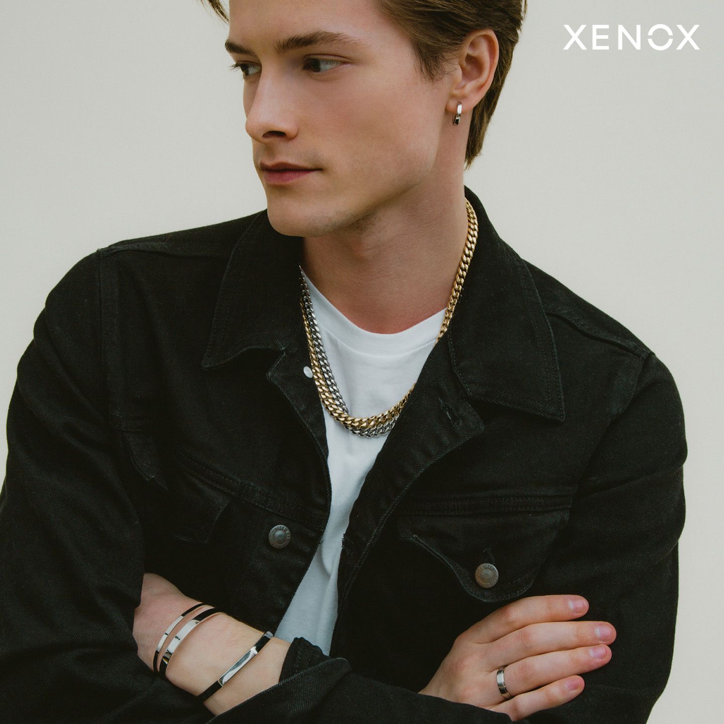 Ein Mann, der eine schwarze Jacke und eine Halskette mit der Aufschrift „Xenox“ auf der Unterseite trägt