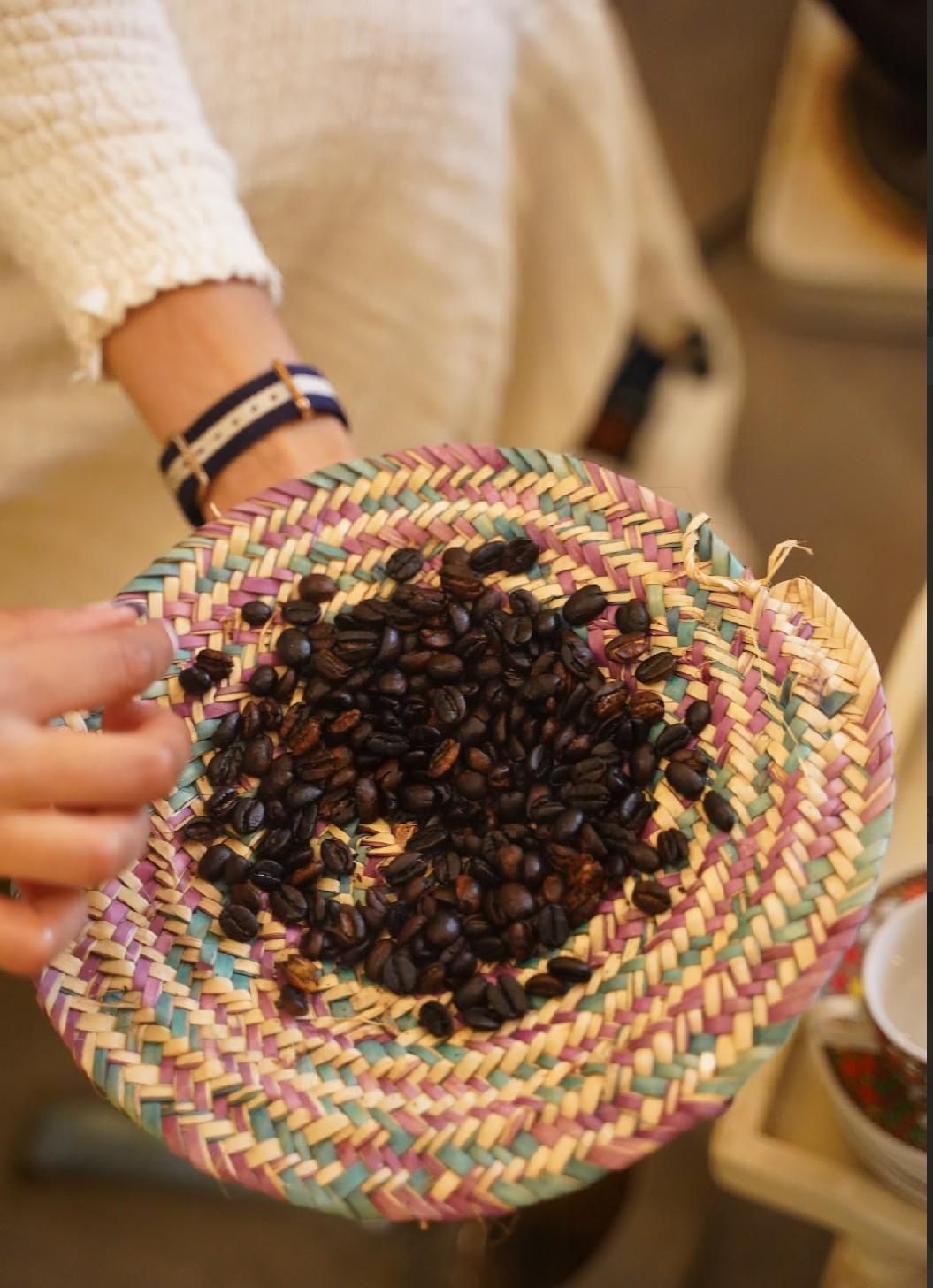 Persona sosteniendo una cesta tejida de granos de café tostado oscuro.