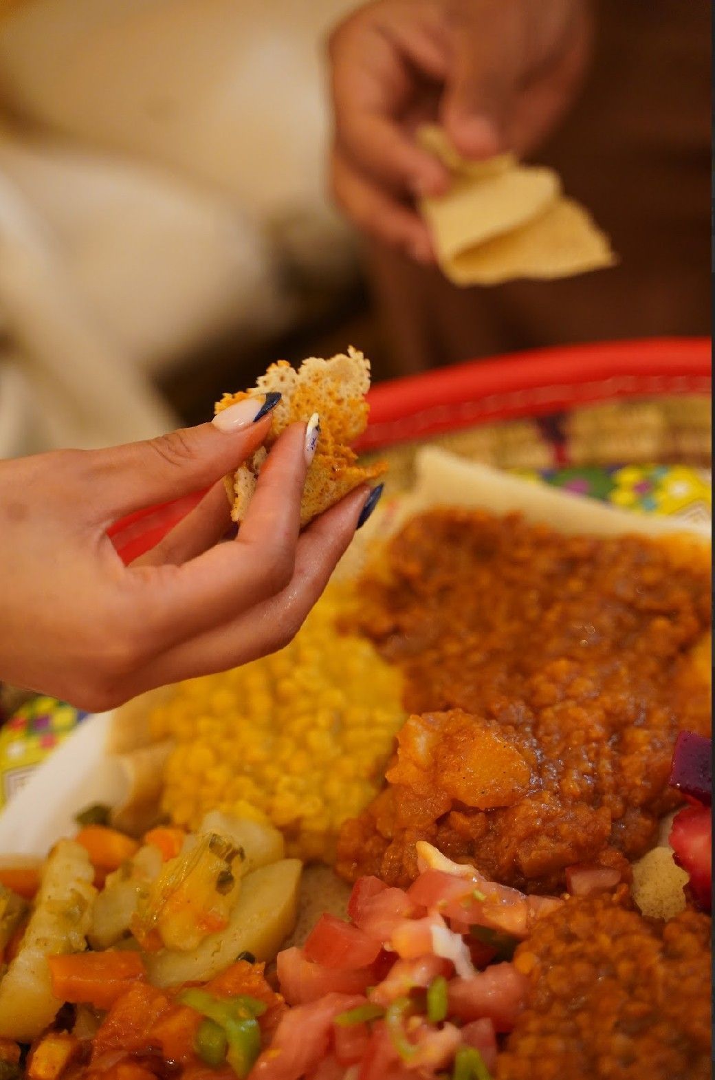 Manos que buscan comida etíope en una bandeja, usando pan injera para comer guiso y verduras.