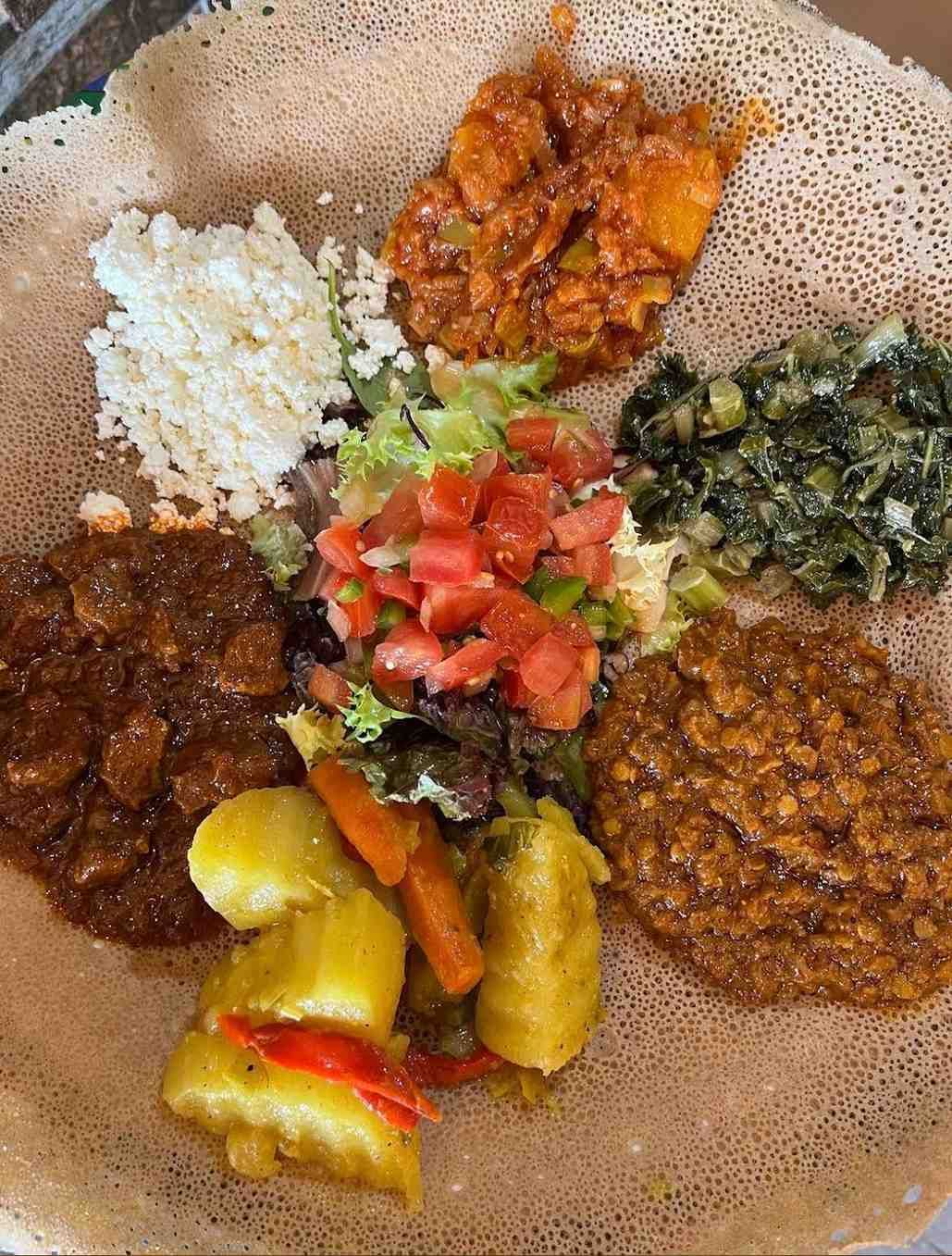 Plato de comida etíope en pan injera. Diversos guisos, verduras y quesos dispuestos en círculo.