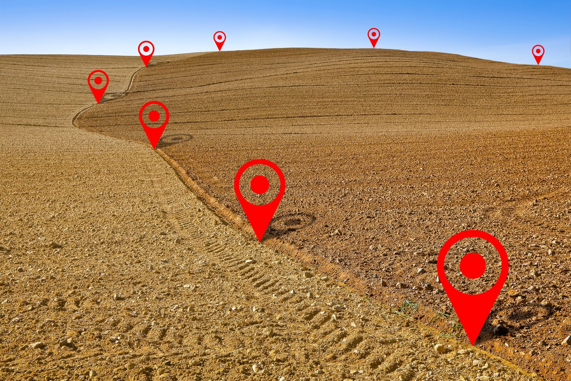 Des balises rouges tracent un chemin incurvé à travers un champ labouré sous un ciel bleu.