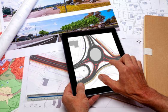 Des mains utilisent une tablette au design circulaire, entourée de cartes et de plans.