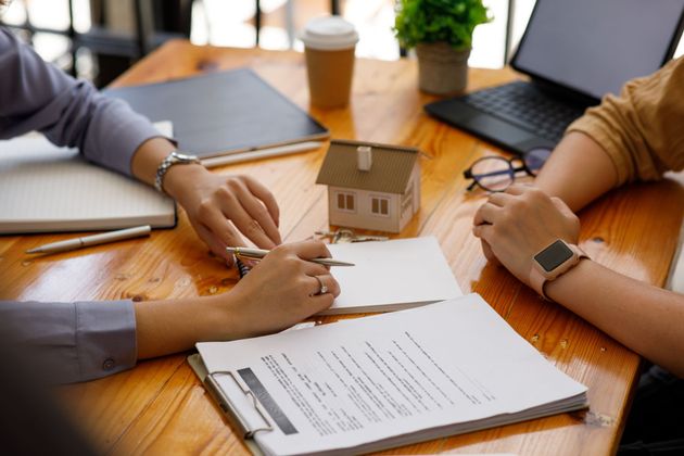 Des personnes signent des documents à une table en bois, à côté d'une maquette de maison.