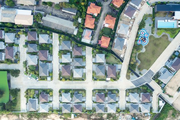 Vue aérienne d'un quartier de banlieue avec des rangées de maisons, des routes et des espaces verts.