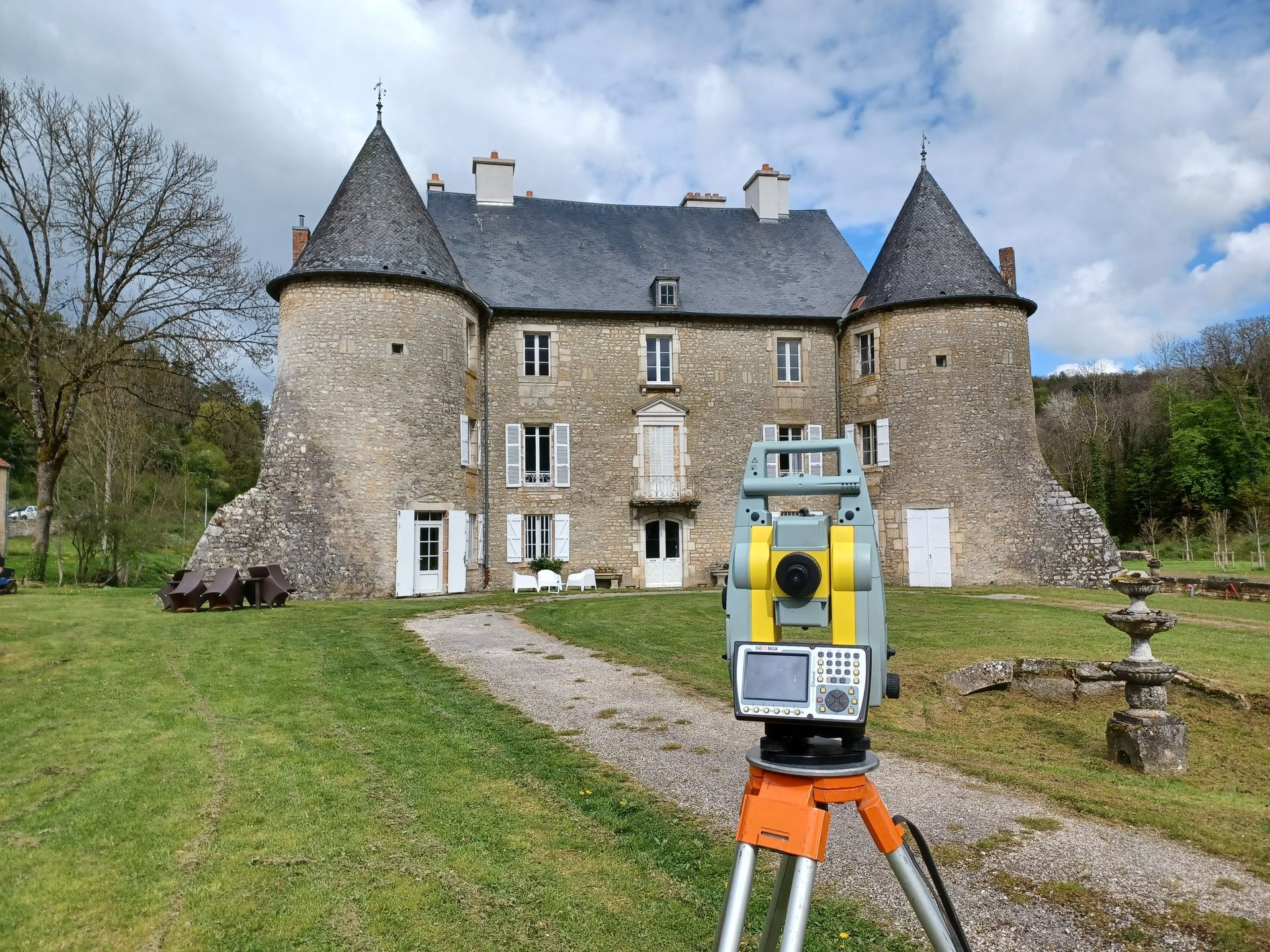 Scanner sur trépied devant un château en pierre avec des tours coniques et un terrain herbeux.
