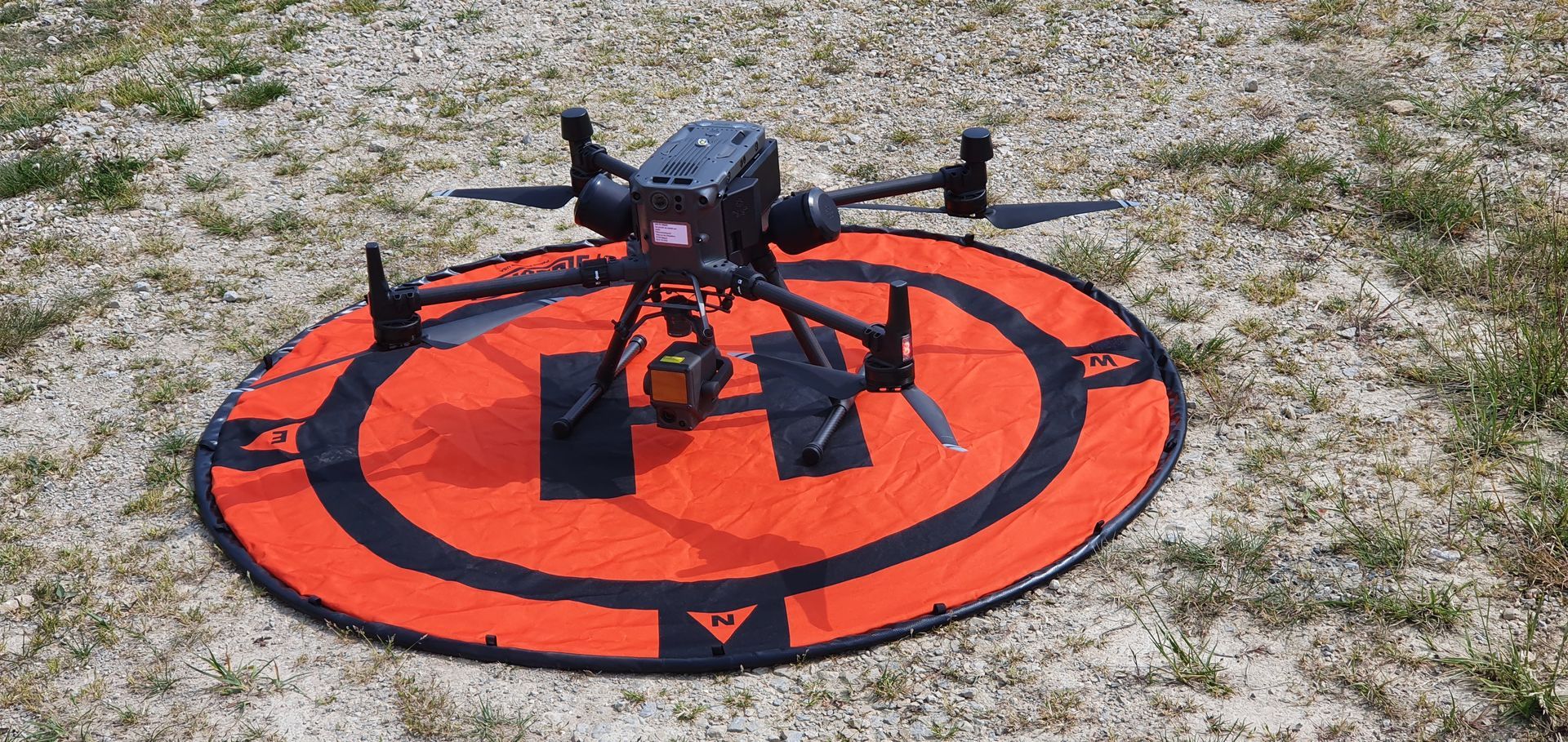 Drone noir sur une plateforme d'atterrissage rouge, en extérieur sur un terrain rocailleux.