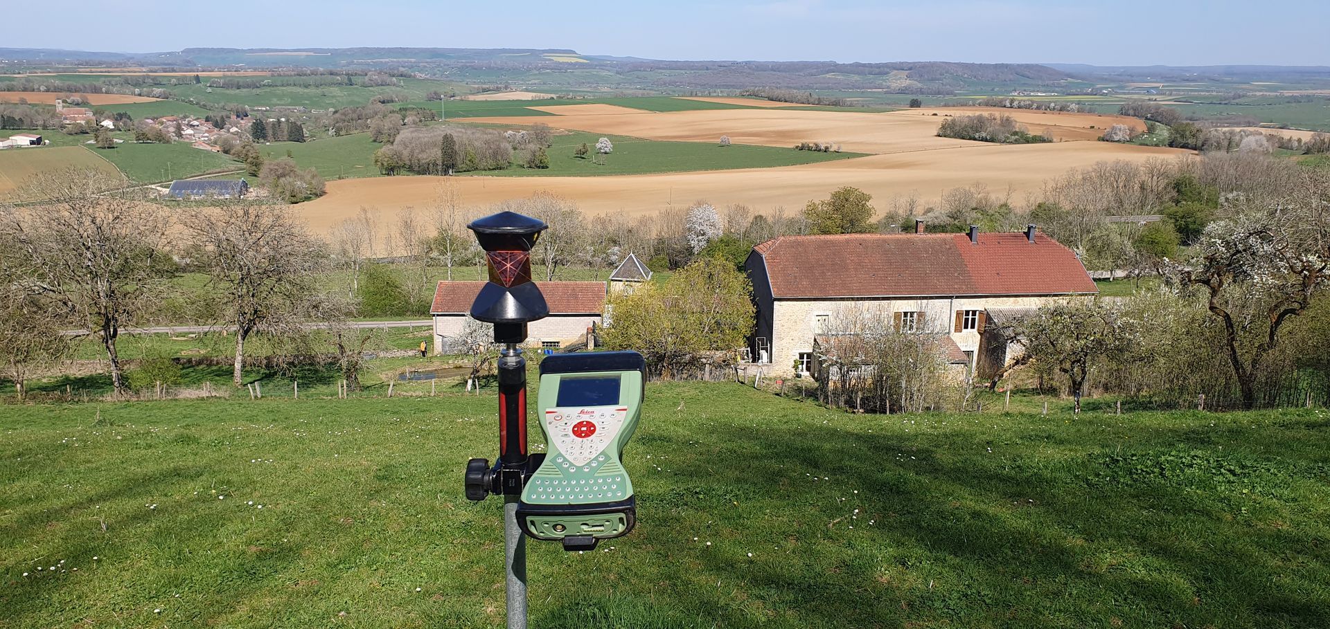 Scanner topographique sur une colline herbeuse surplombant une vallée rurale et des champs.