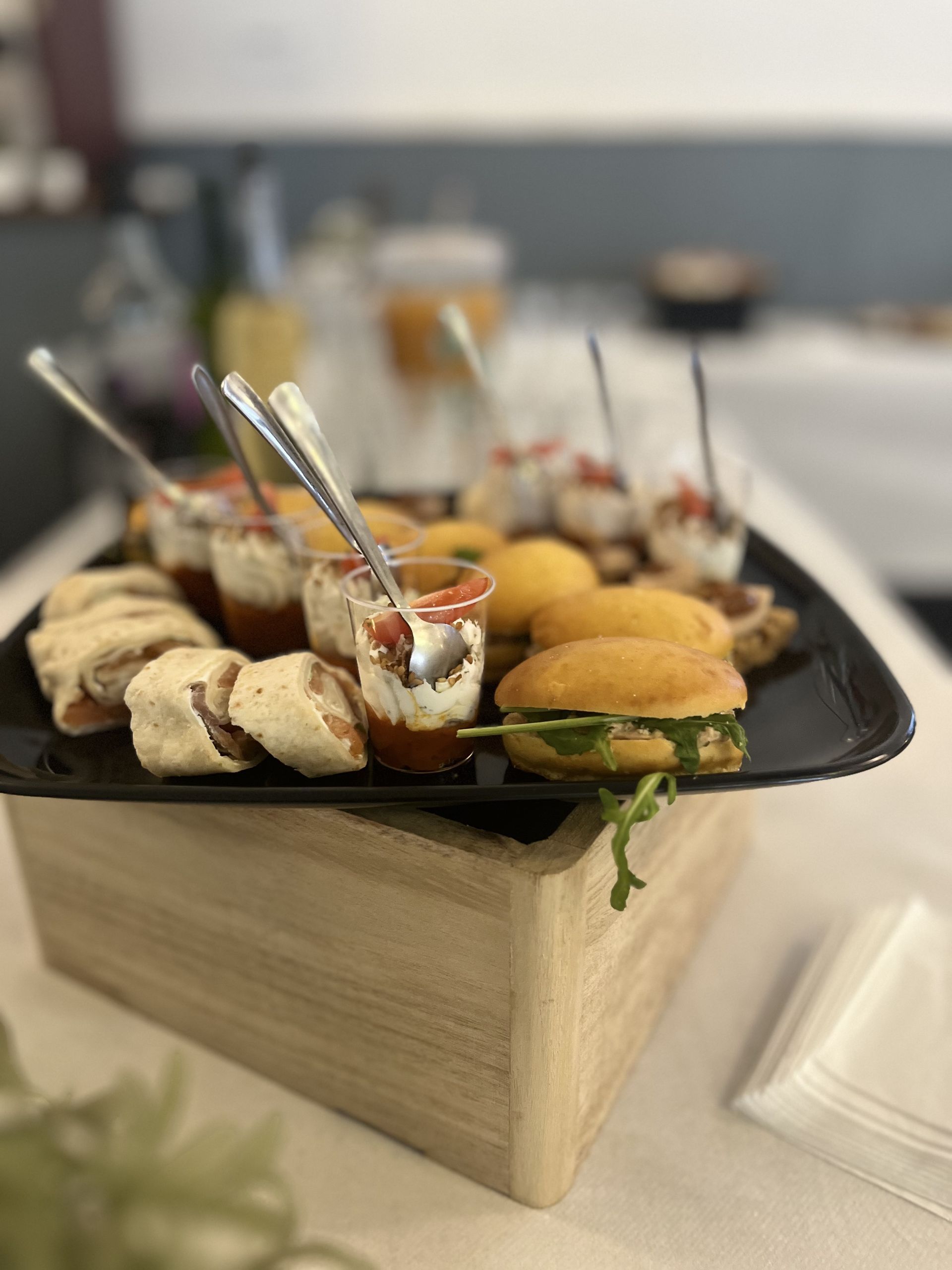 Plateau d'amuse-gueules sur un support en bois. Wraps, mini-sandwichs et desserts à étages avec cuillères.