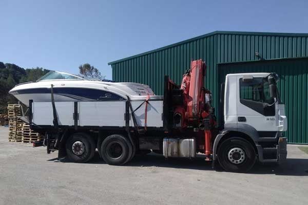 Un camión blanco con una grúa en la parte trasera transporta un barco.