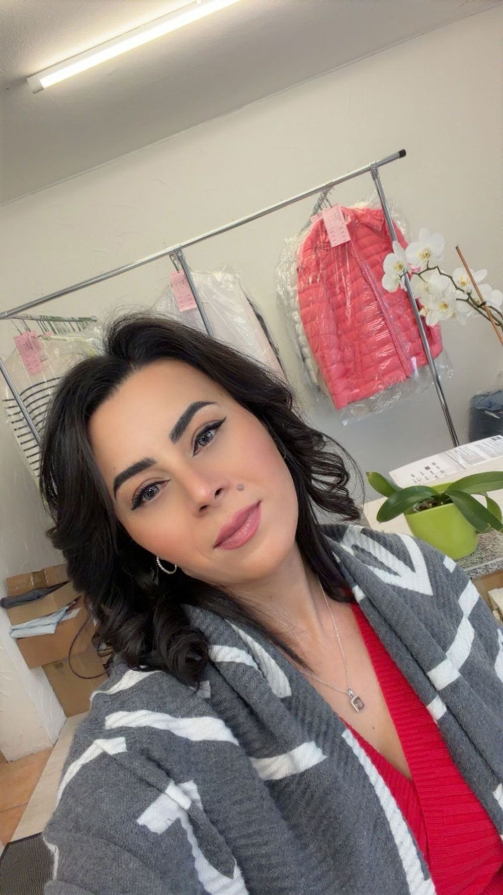 Frau in grau-weiß gestreiftem Pullover und rotem Oberteil. Sie blickt in die Kamera. Im Hintergrund: eine chemische Reinigung.