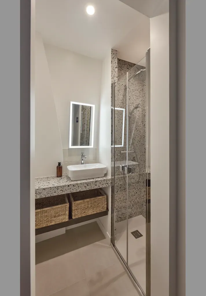 Salle de bains avec lavabo blanc, douche en mosaïque, paniers sous le meuble-lavabo.