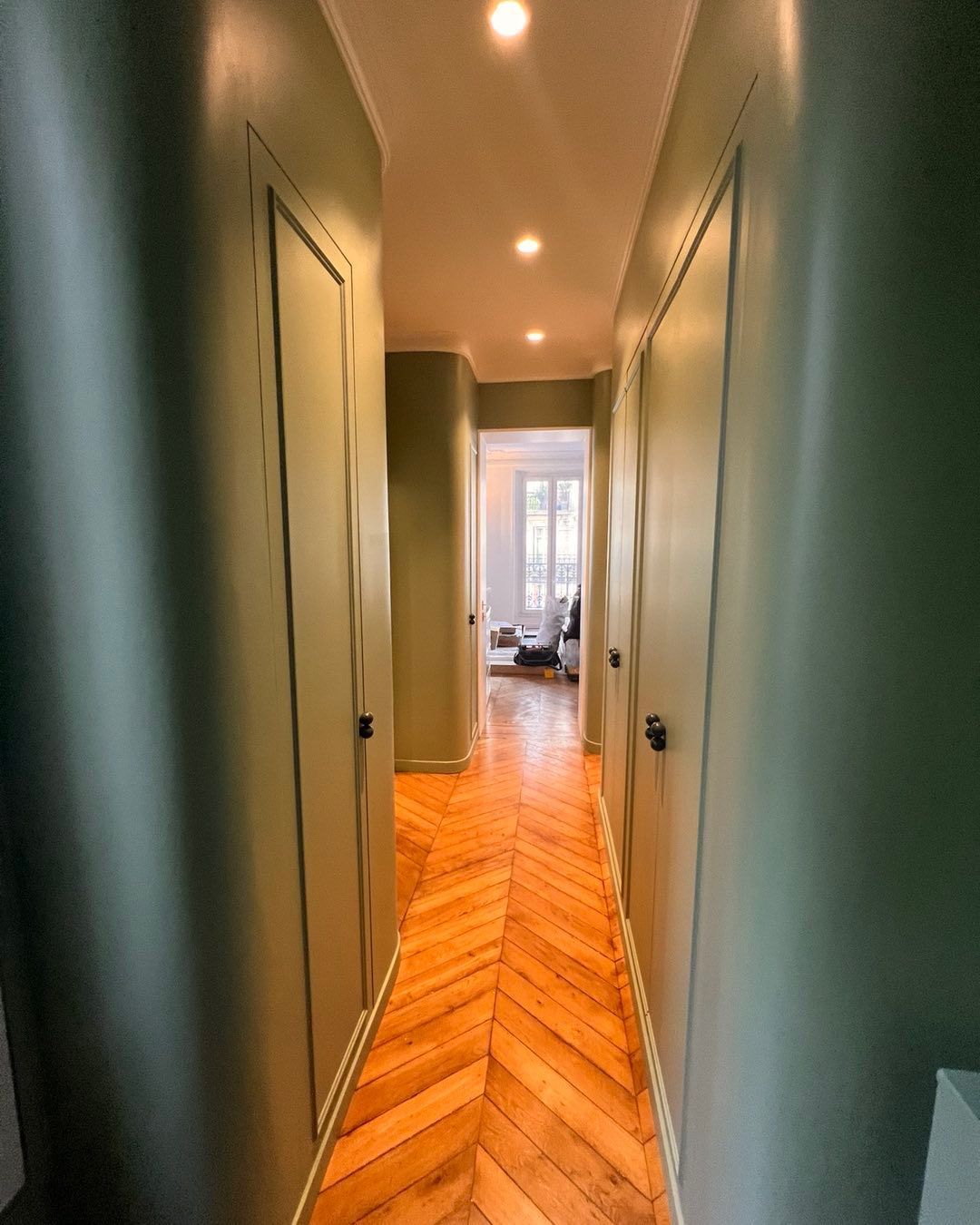 Couloir aux murs verts, portes fermées et parquet en chevrons.