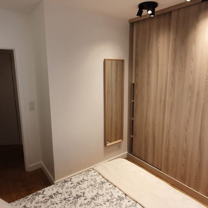 Chambre avec armoire en bois et miroir mural ; lit avec couvre-lit à motifs.
