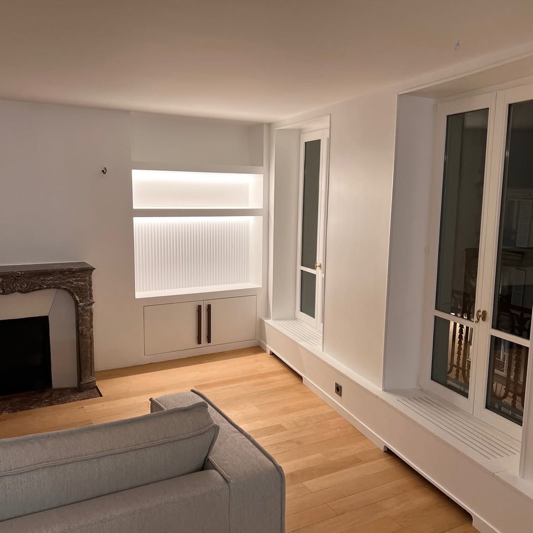 Salon avec cheminée, rangements intégrés, parquet clair et grandes fenêtres.