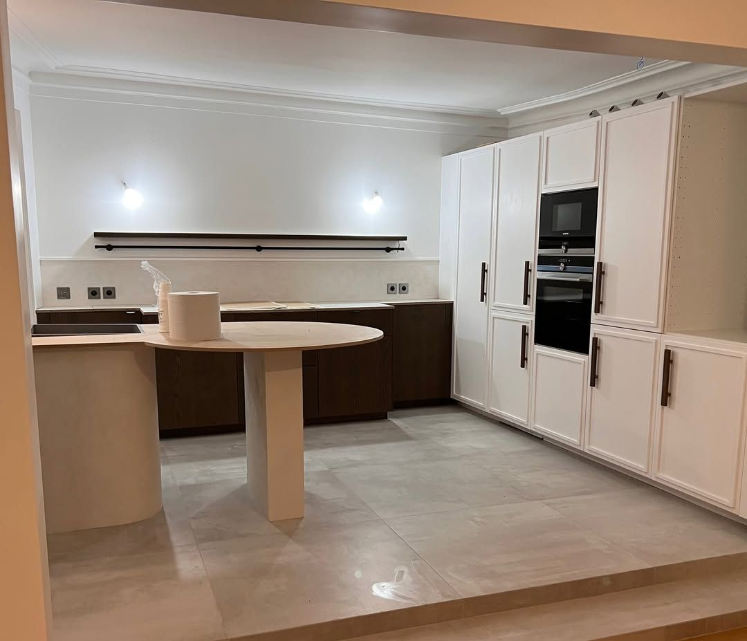 Cuisine moderne avec placards blancs, comptoir marron foncé et sol carrelé gris clair.