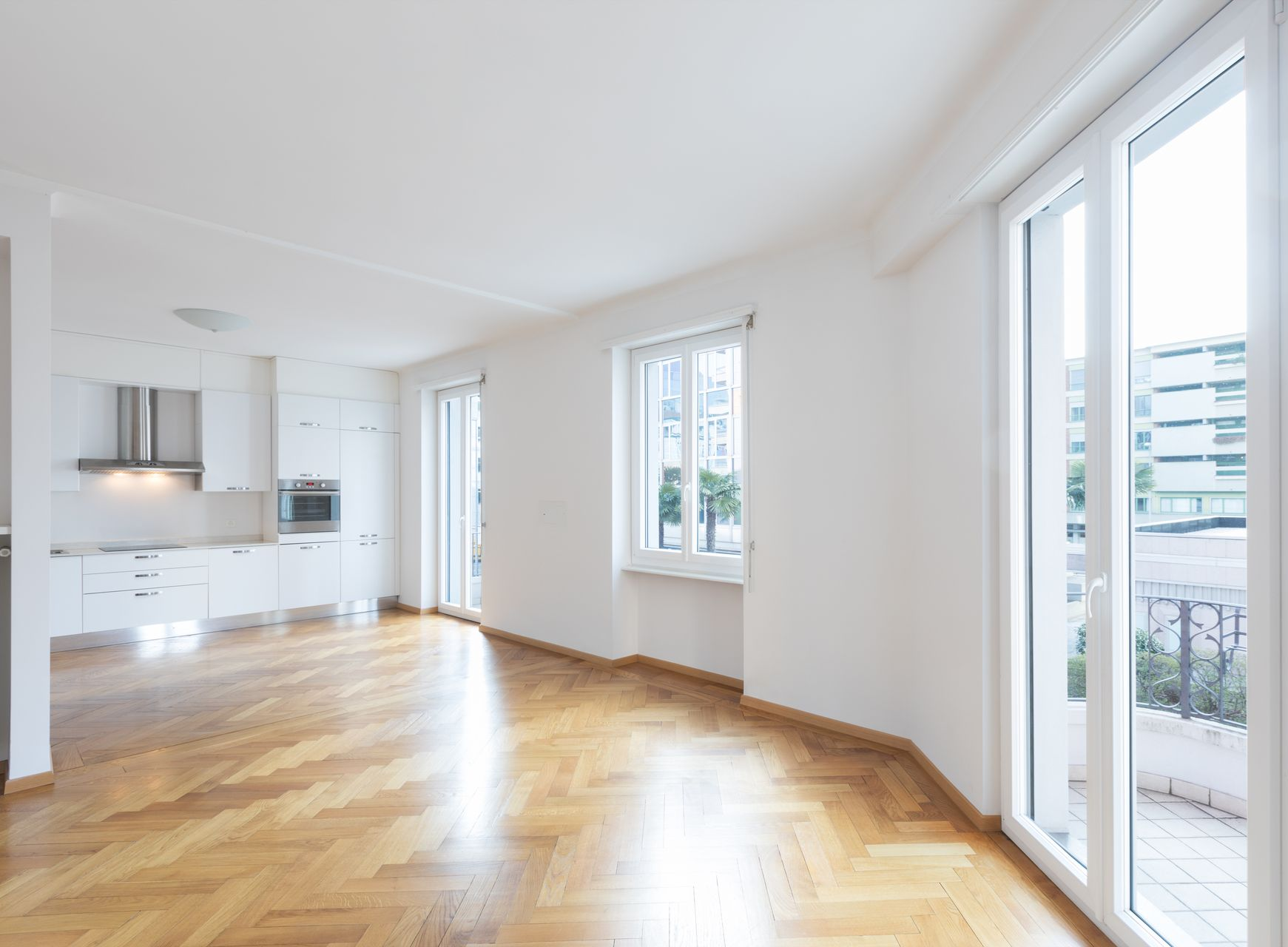 Espace de vie lumineux avec parquet, murs et cuisine blancs et grandes fenêtres.