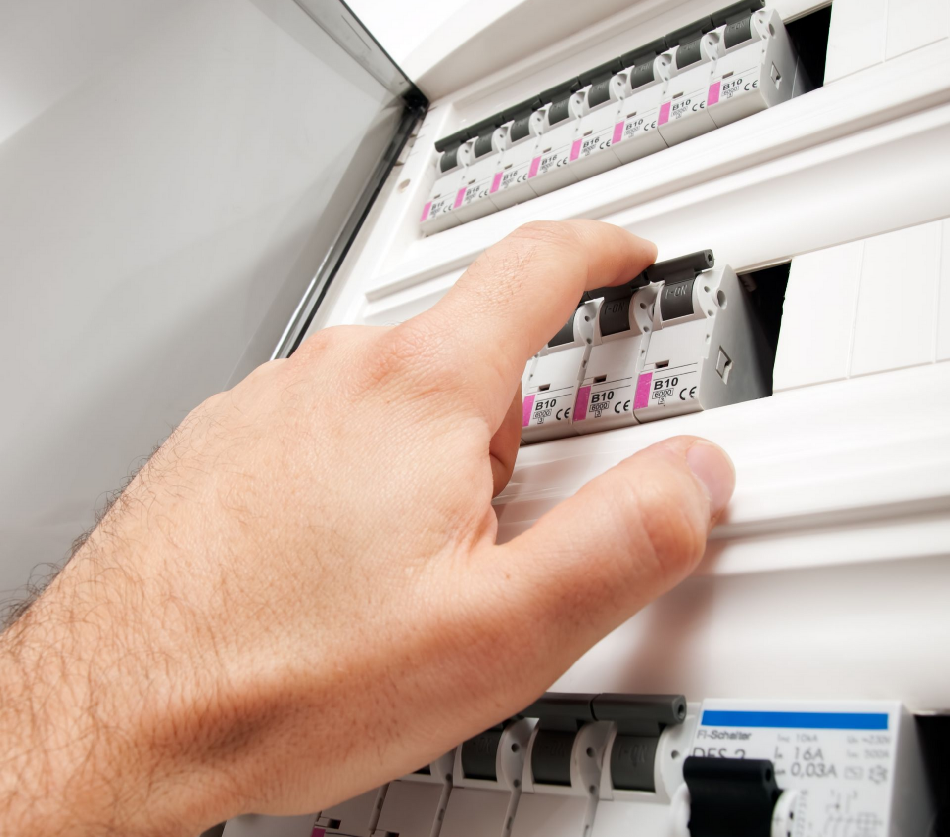 Une main tendue pour actionner le disjoncteur du tableau électrique blanc.