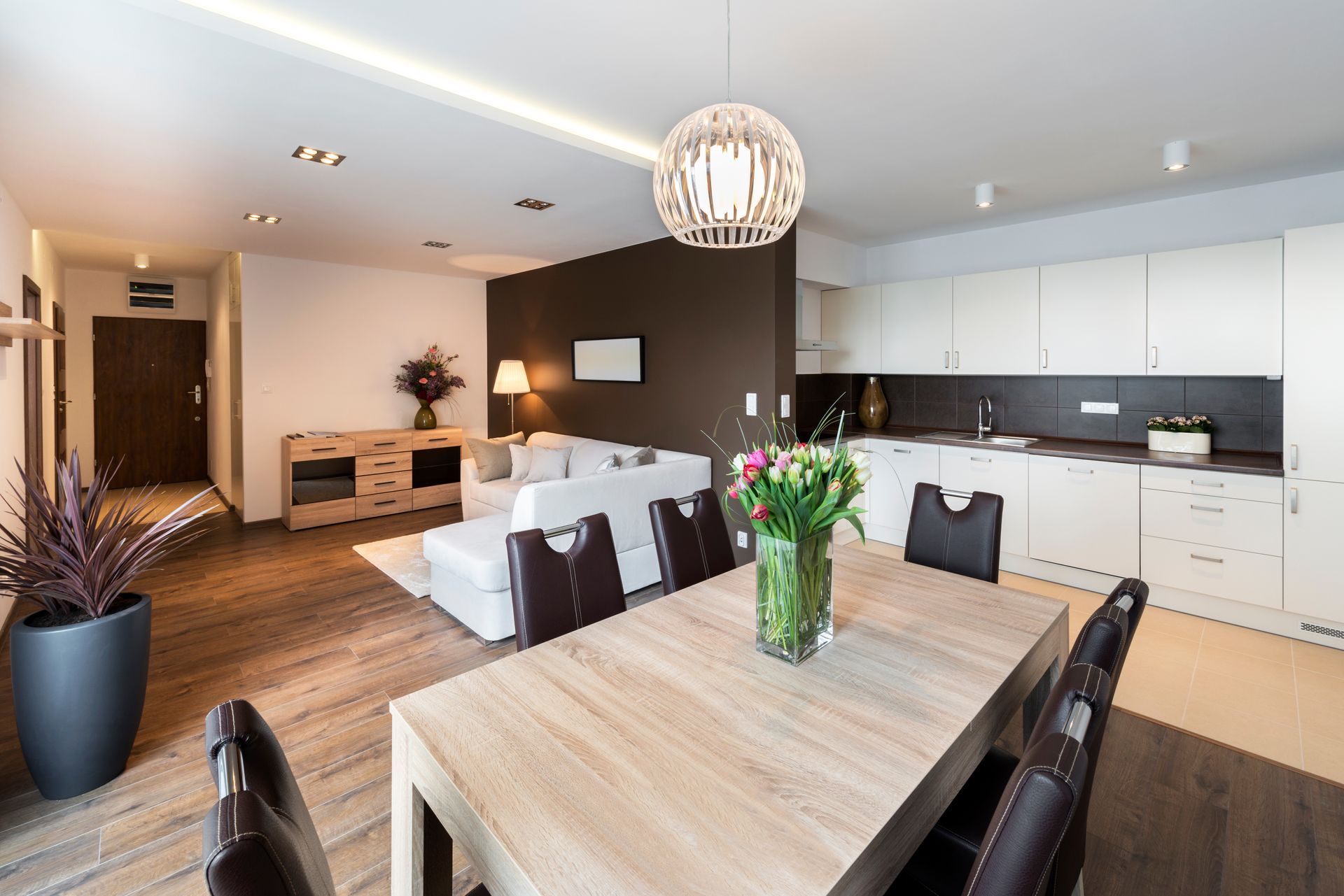 Espace de vie moderne et ouvert comprenant une cuisine, une table à manger et un canapé. Tons bruns, blancs et boisés.