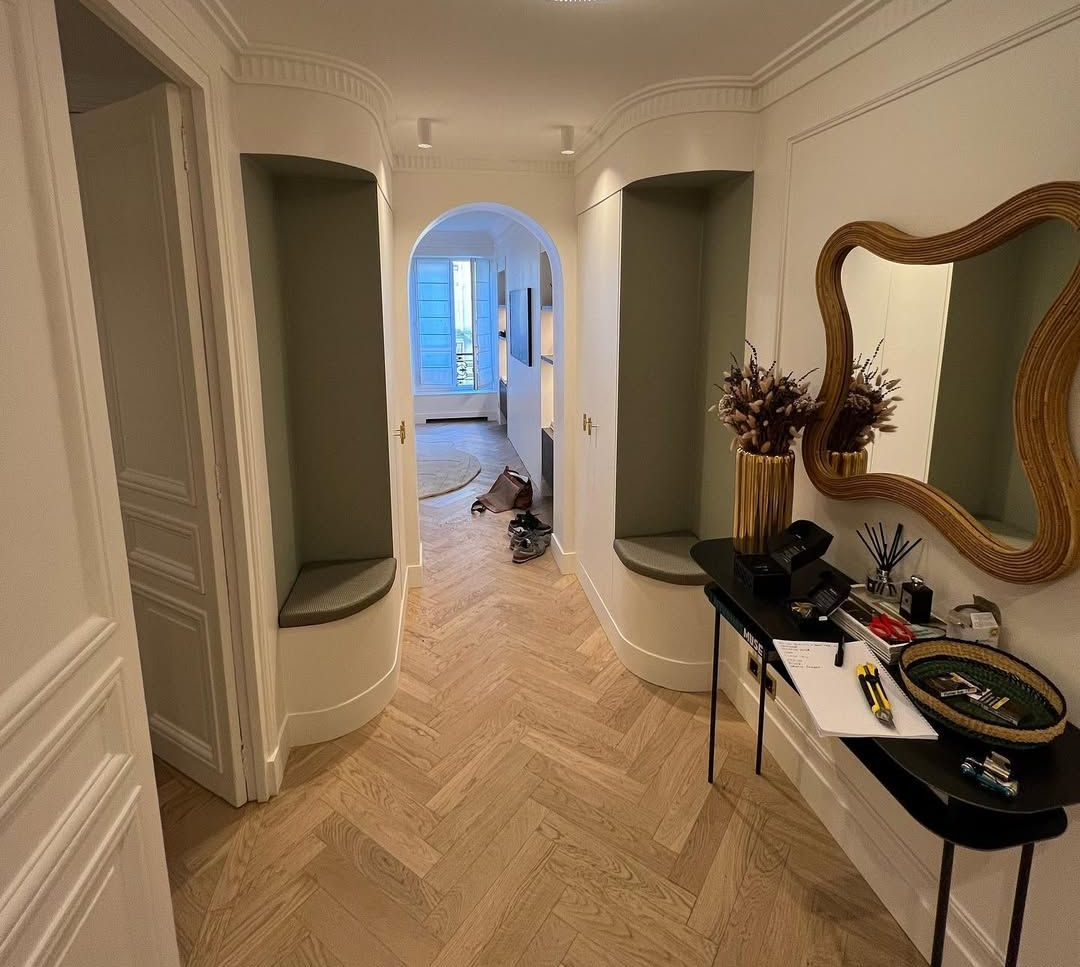 Couloir avec alcôves cintrées, parquet à chevrons et miroir à cadre doré.