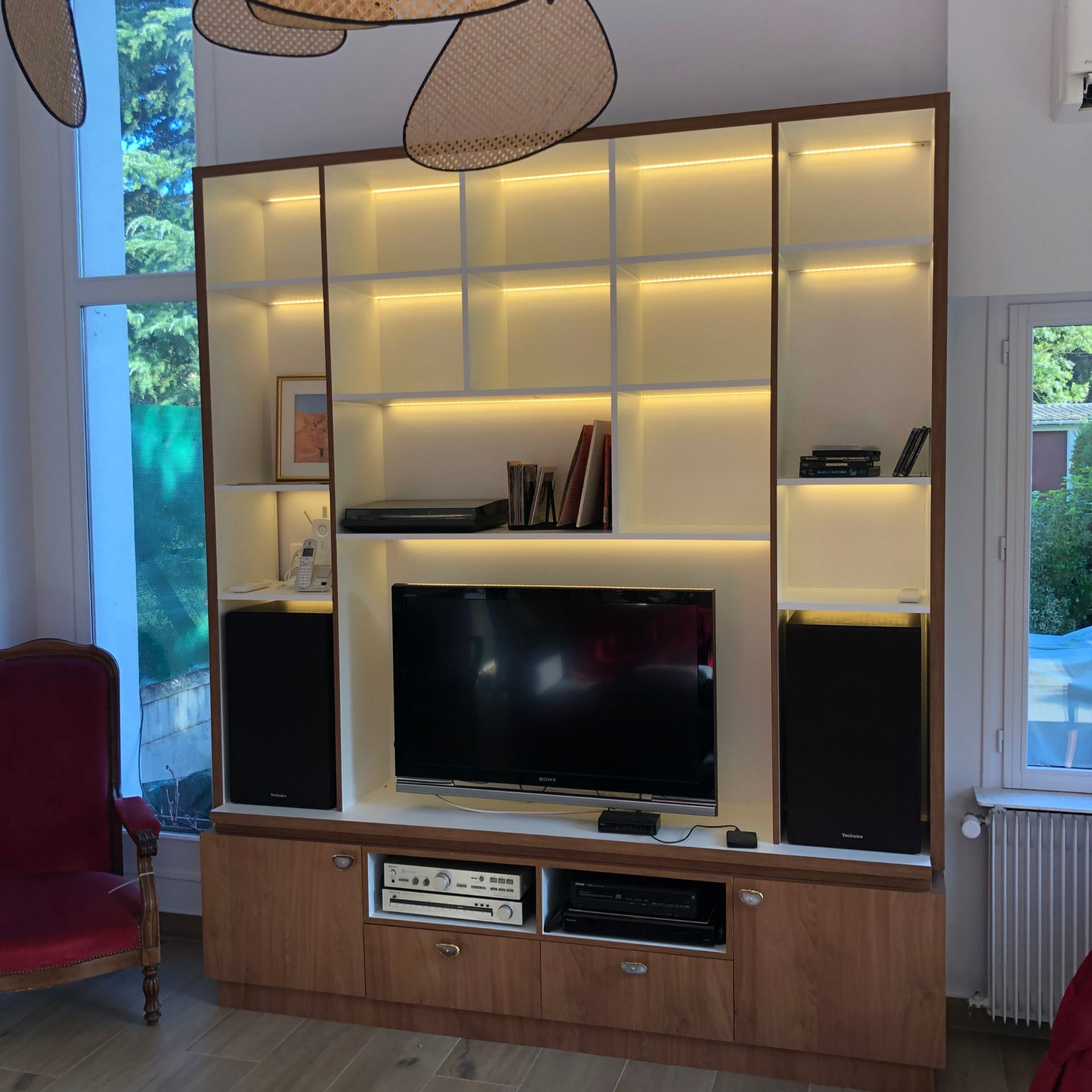 Meuble TV intégré avec télévision et étagères éclairées, à côté d'une fenêtre.