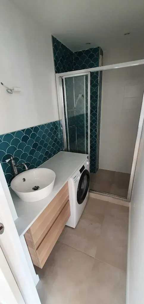 Salle de bains avec crédence en carrelage turquoise à écailles de poisson, plan de travail blanc, lavabo.
