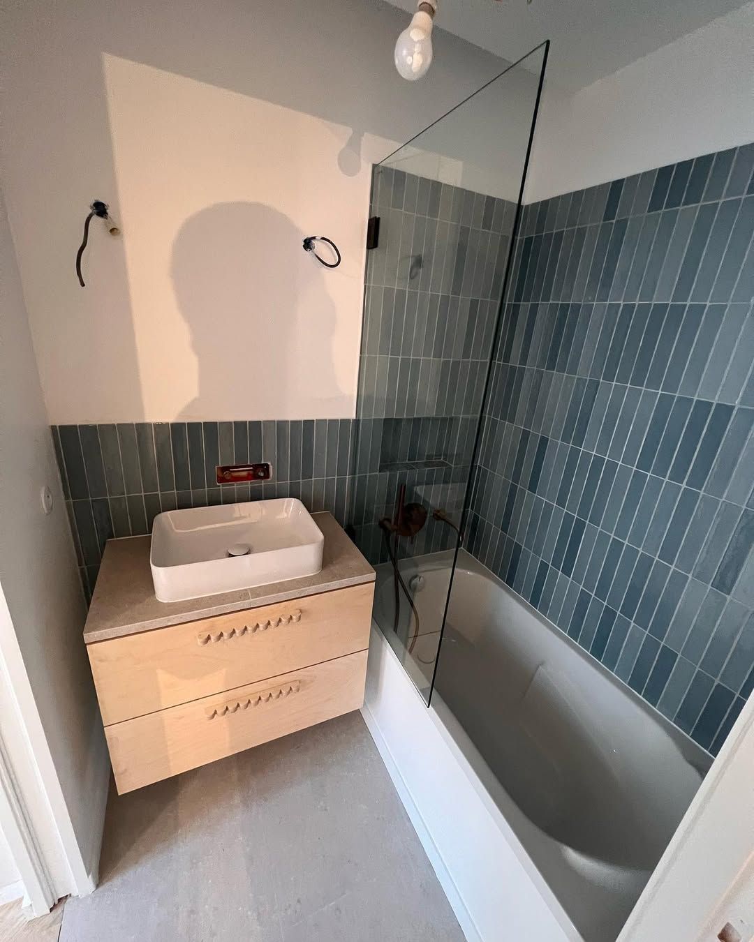 Salle de bains avec baignoire, meuble en bois clair et carrelage bleu.