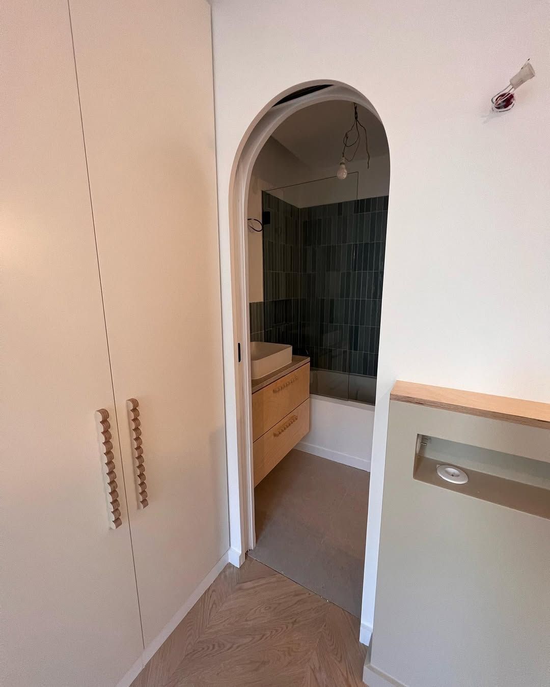 Porte de salle de bains avec entrée cintrée donnant sur le meuble-lavabo, la douche et le placard. Murs blancs, parquet.