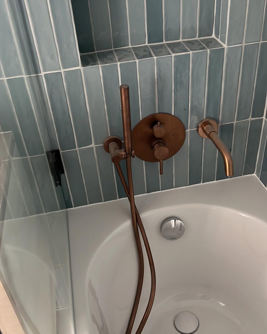 Robinetterie de douche couleur cuivre et baignoire avec du carrelage bleu clair.