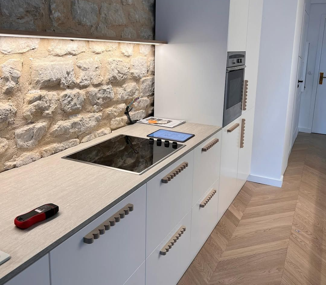 Cuisine moderne avec mur en pierre, placards blancs et électroménager intégré.