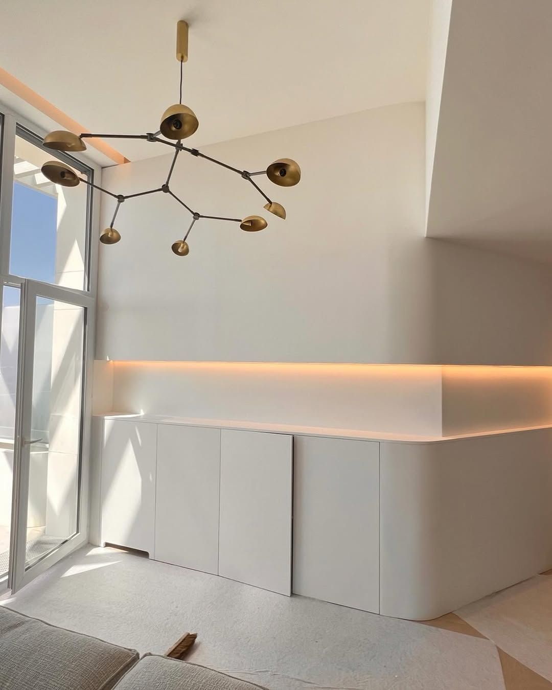 Chambre blanche moderne avec rangements intégrés, luminaire décoratif et grande fenêtre.