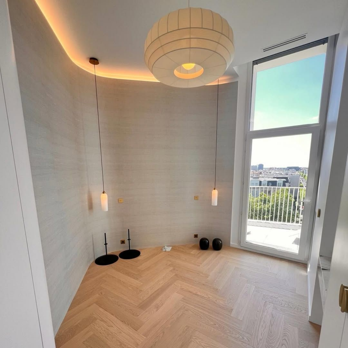 Pièce avec parquet, grande fenêtre et éclairage moderne.