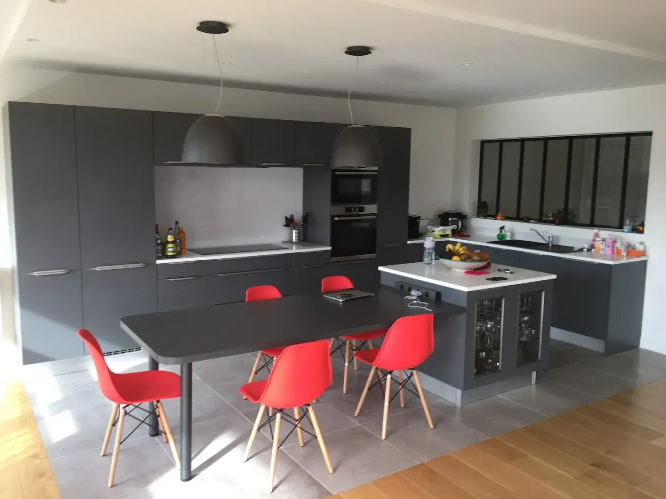 Cuisine moderne noire avec des chaises rouges autour d'une table et un îlot central.