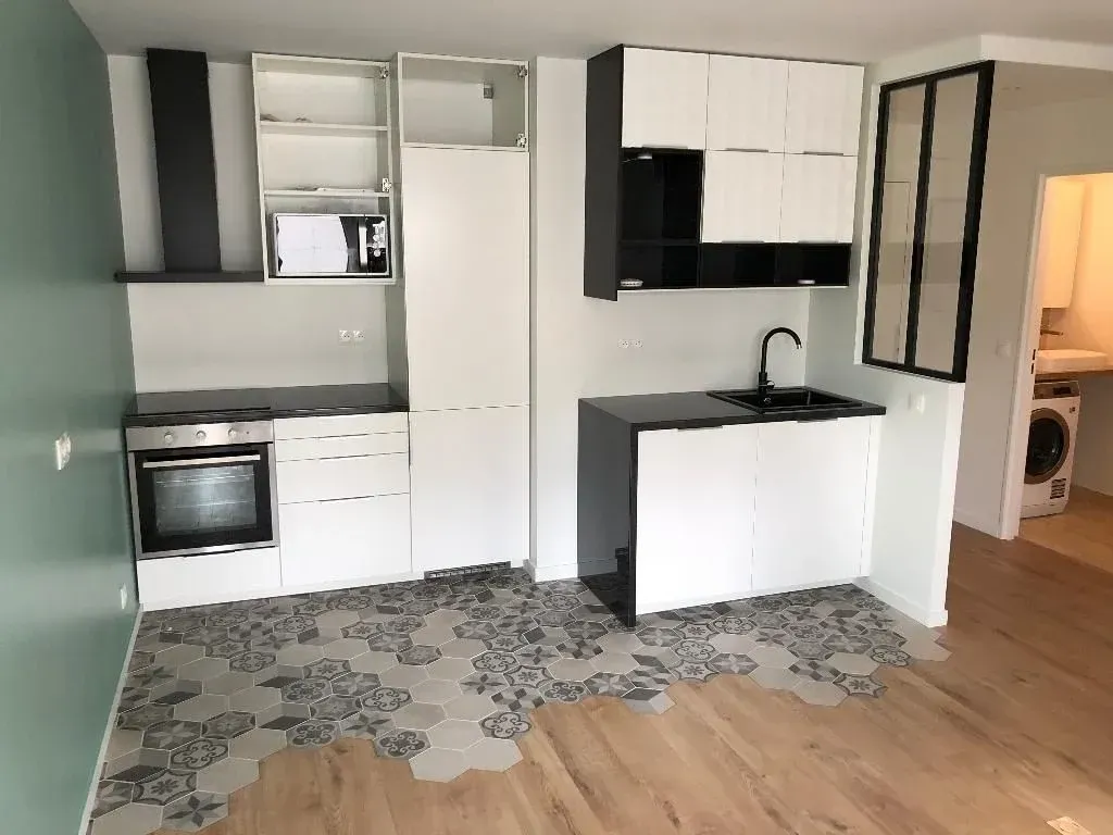 Petite cuisine moderne avec placards blancs et noirs, four et micro-ondes.