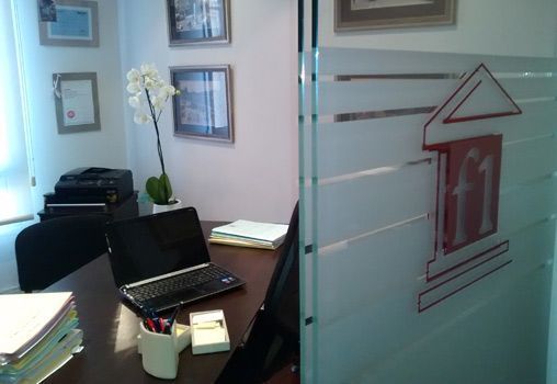 Una computadora portátil está sobre un escritorio frente a una ventana con un logotipo de F1 en ella.