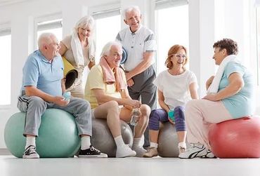 Un grupo de personas mayores están sentadas sobre pelotas de ejercicio en un gimnasio.