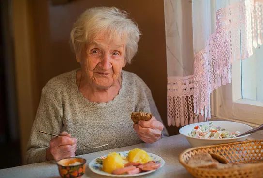 Una mujer mayor está sentada en una mesa comiendo comida.