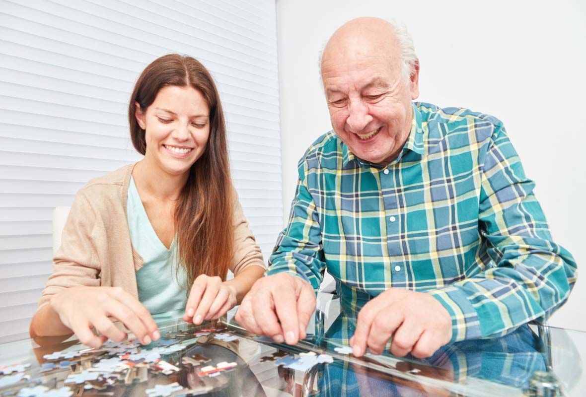 Un hombre mayor y una mujer joven están jugando un rompecabezas juntos.