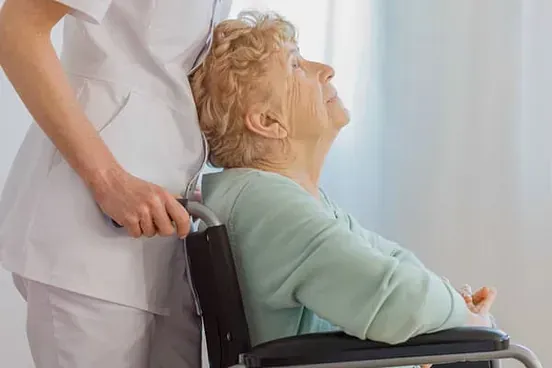 Una anciana en silla de ruedas recibe ayuda de una enfermera.