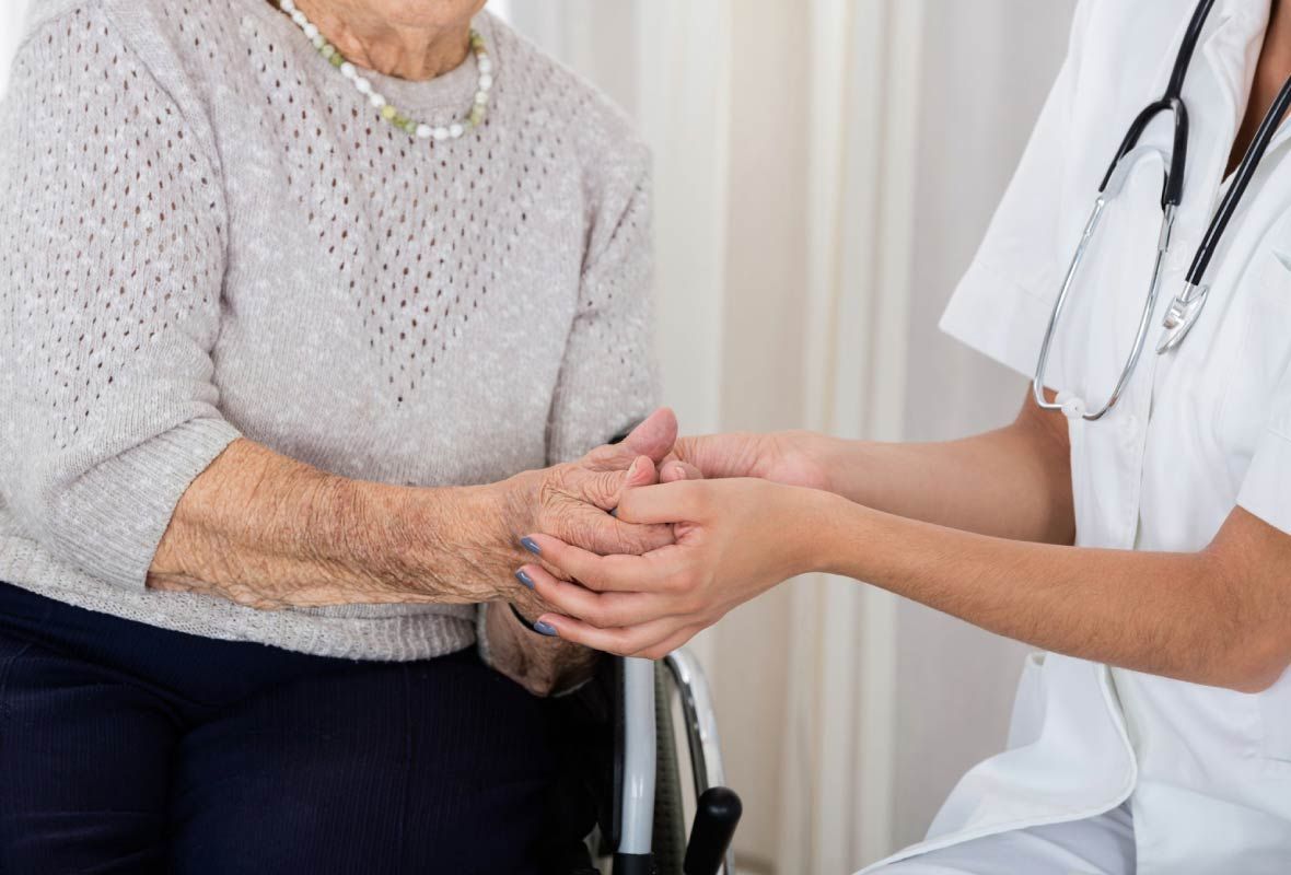 Una enfermera sostiene la mano de una anciana en silla de ruedas.