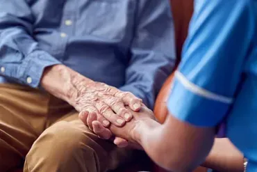 Una enfermera sostiene la mano de un anciano.