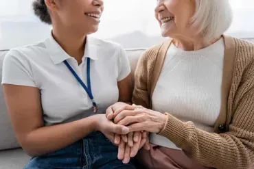 Una enfermera sostiene las manos de una anciana en un sofá.