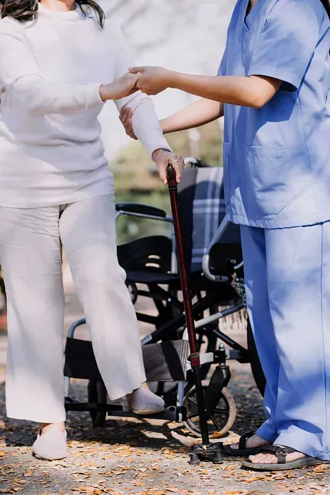 Una enfermera está ayudando a una anciana en silla de ruedas a caminar.