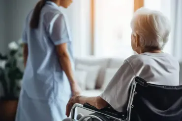 Una enfermera camina con una anciana en silla de ruedas.