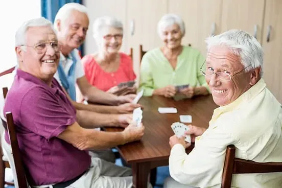 Un grupo de personas mayores están sentadas alrededor de una mesa jugando a las cartas.