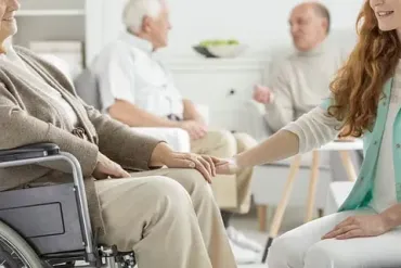 Una mujer sostiene la mano de una anciana en silla de ruedas.