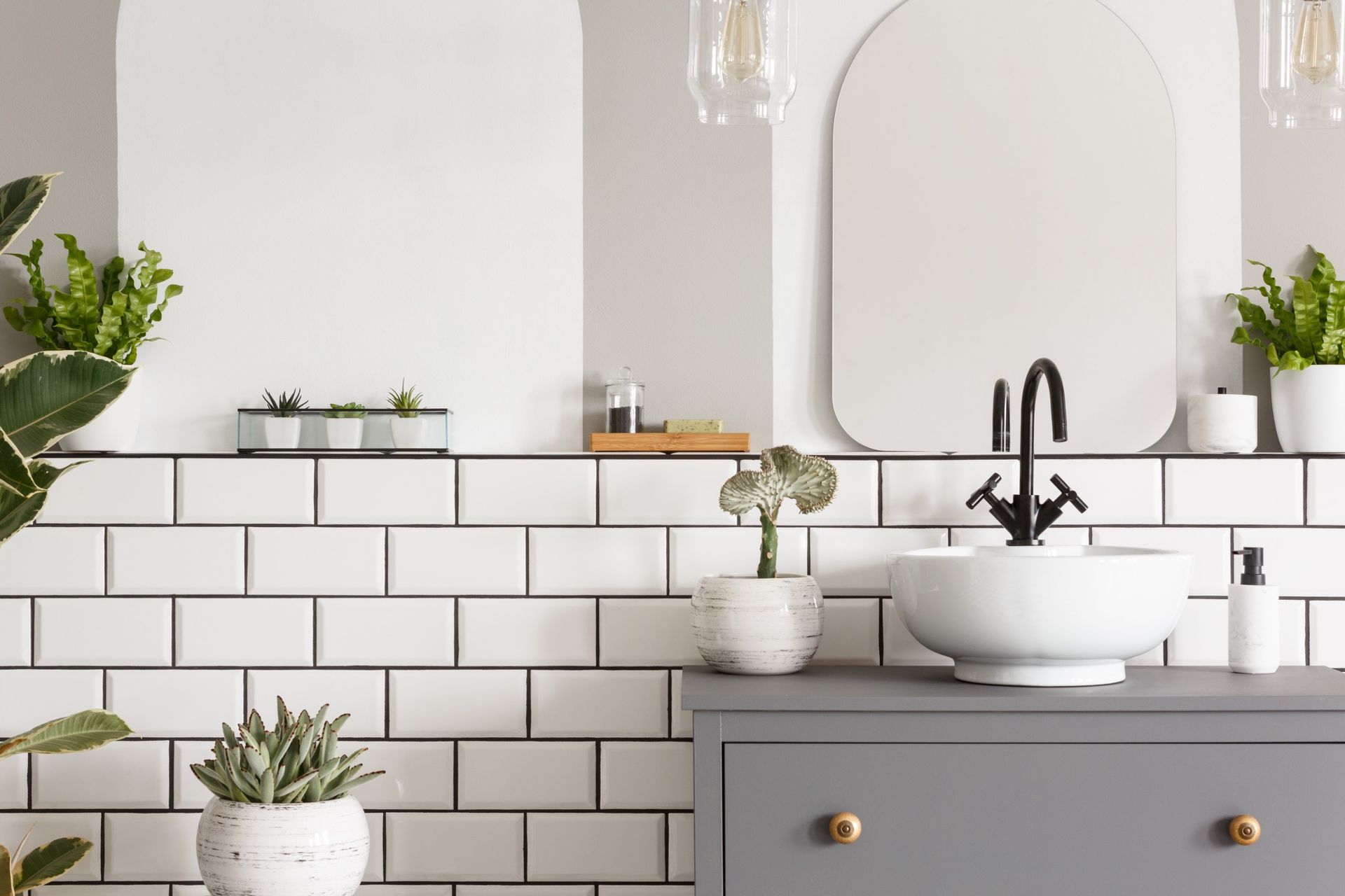 Un baño con azulejos blancos, un lavabo, un espejo y plantas en macetas.
