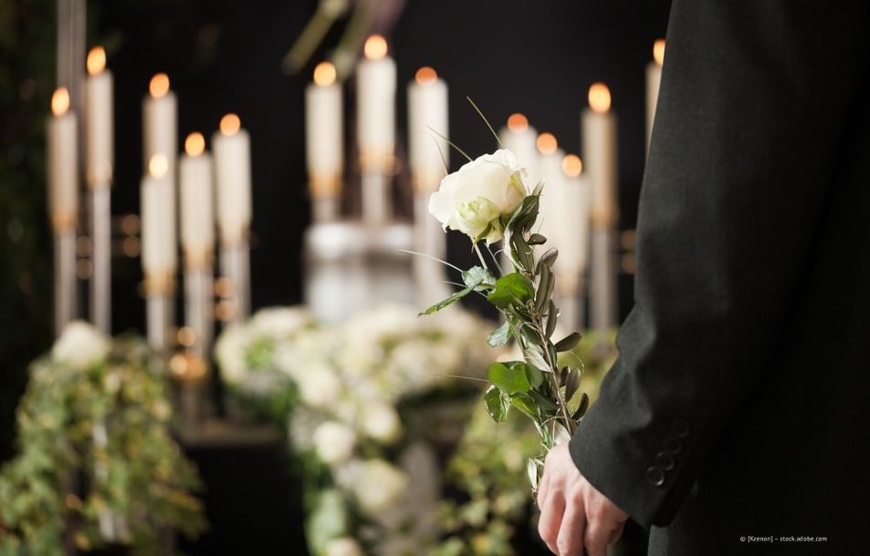 Eine Person in Schwarz hält weiße Blumen neben brennenden Kerzen an einer schwach beleuchteten Gedenkstätte.