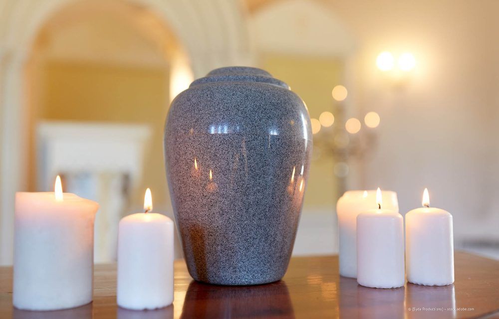 Eine dekorative Vase, umgeben von brennenden weißen Kerzen, steht auf einem Tisch in einem sanft beleuchteten Raum.