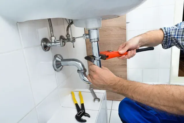 Un fontanero está arreglando un lavabo en un baño con una llave inglesa.